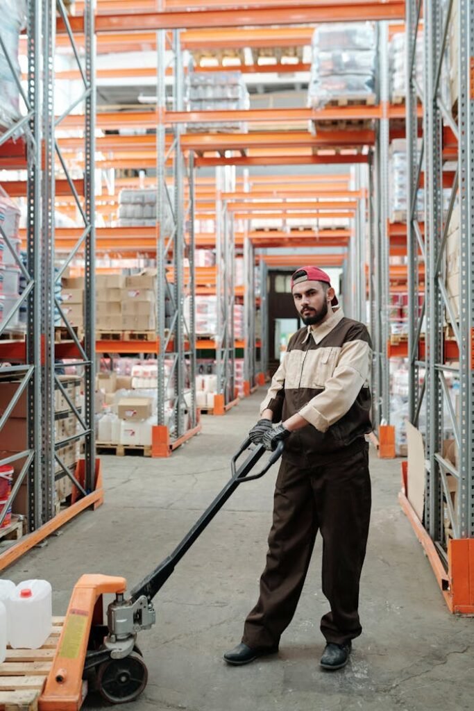 pexels-photo-4487384 Man in uniform using a pallet jack in a well-organized warehouse storeroom.