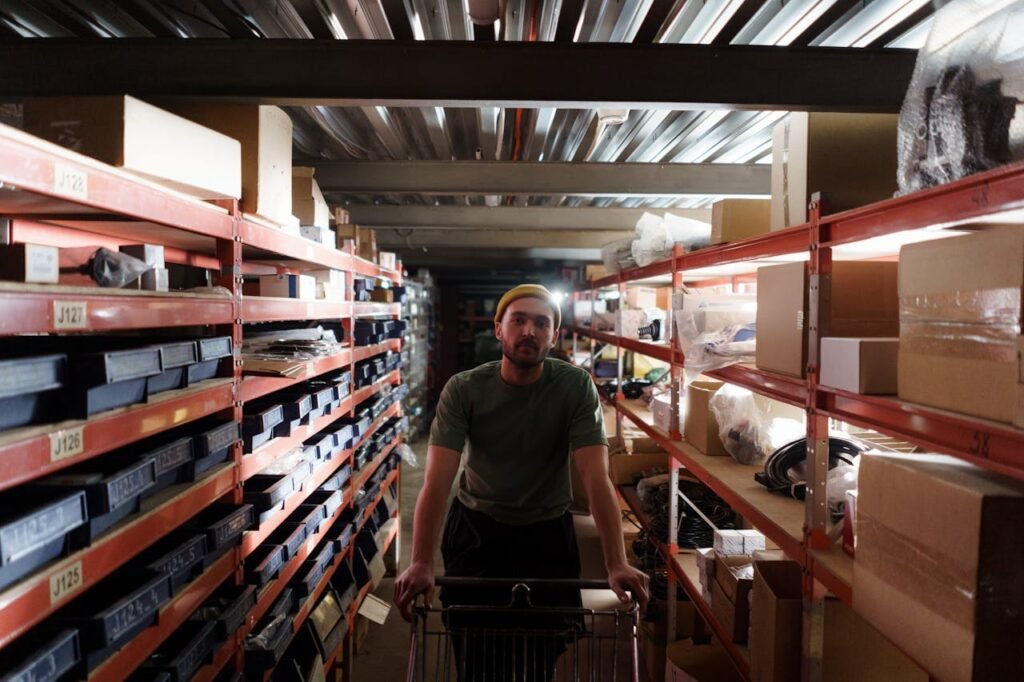 pexels-photo-7019319 A man moves a cart through a busy warehouse aisle lined with shelves and boxes.